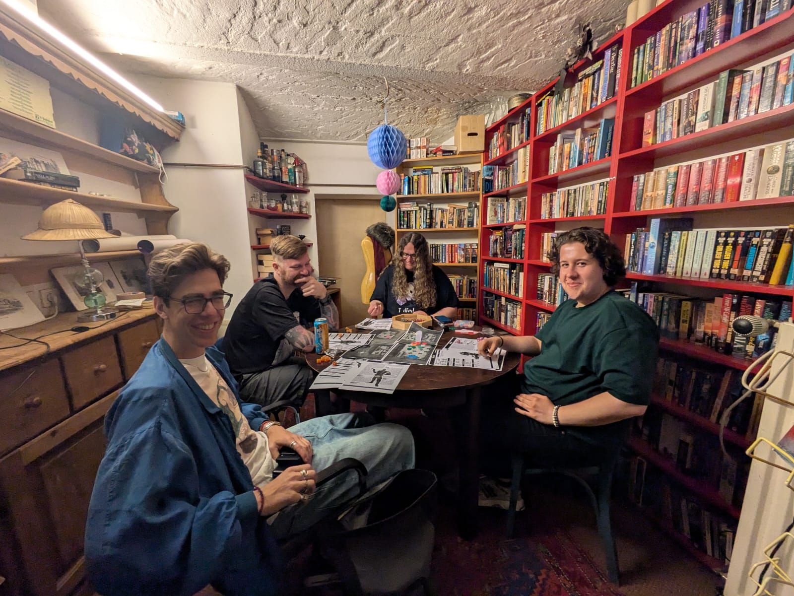 Four players at a round table with printed character sheets spread across it.