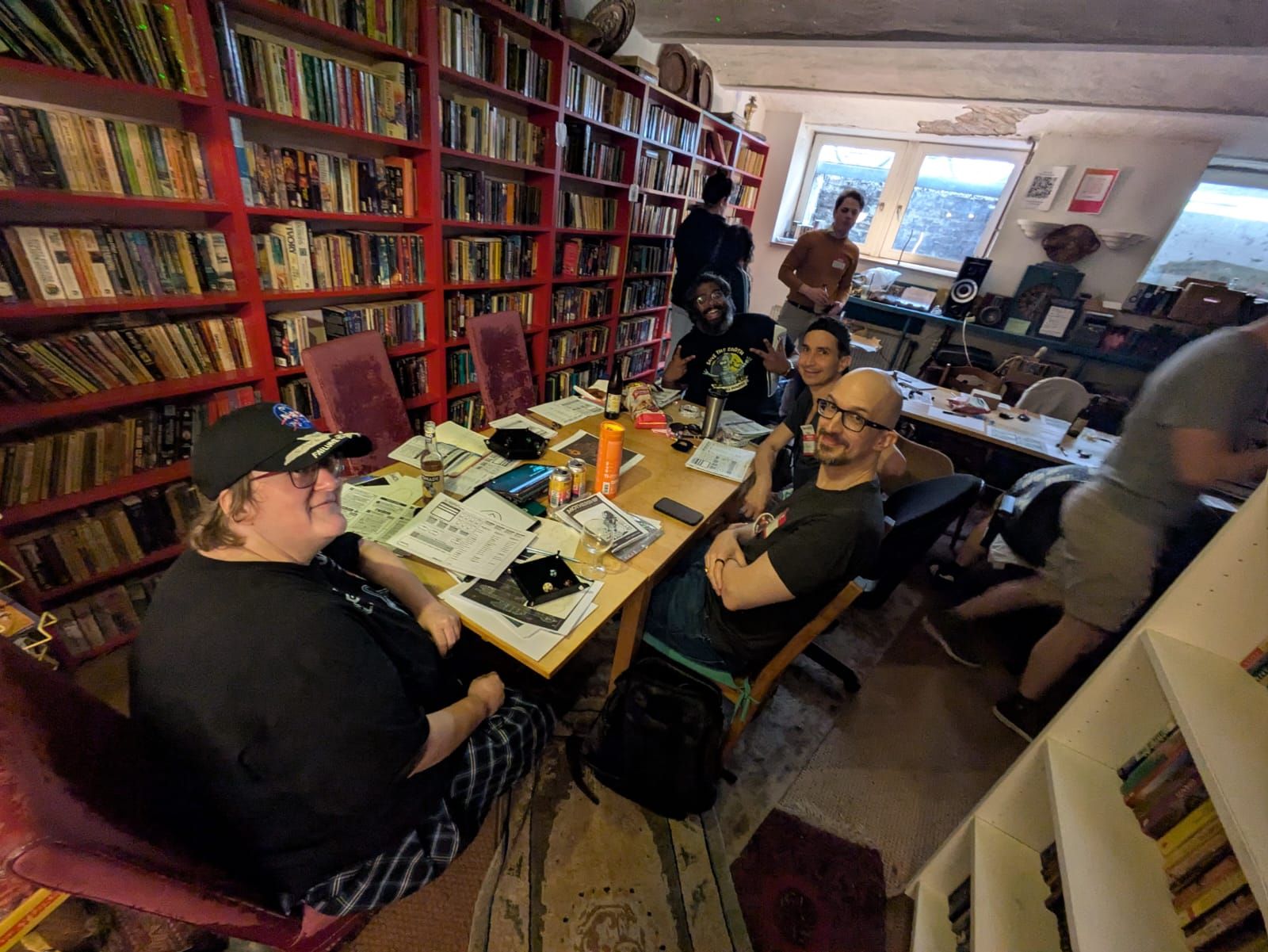 Six players at a table wearing hand-written name badges, character sheets and dice trays in front of them.