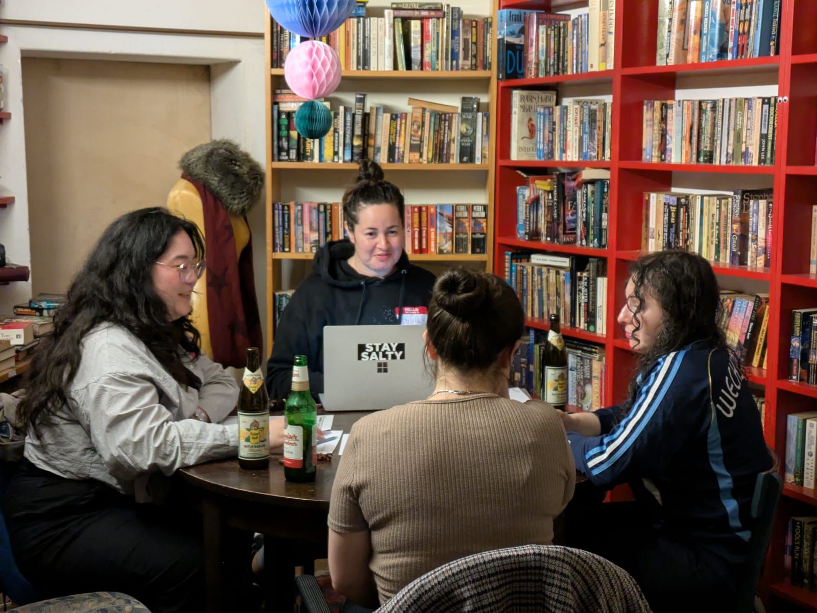 Four people at a small round table, one behind a laptop, beer bottles and a name badge.